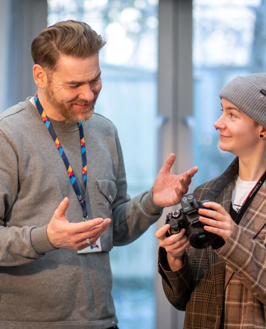 Lecturer chatting with a student holding a DSLR camera in a photography studio. Lecturer chatting with a student holding a DSLR camera in a photography studio.